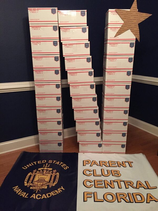 Stacks of Priority Mail care package boxes ready to ship, next to the club banner