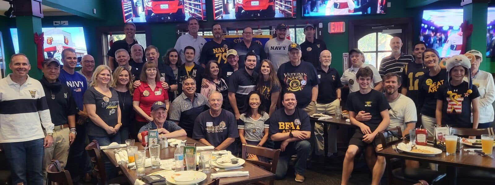 A large group of club families wearing Navy gear together at a restaurant gathering
