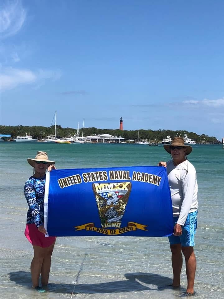 A Class Crest Flag held up on a beach with a lighthouse in the background