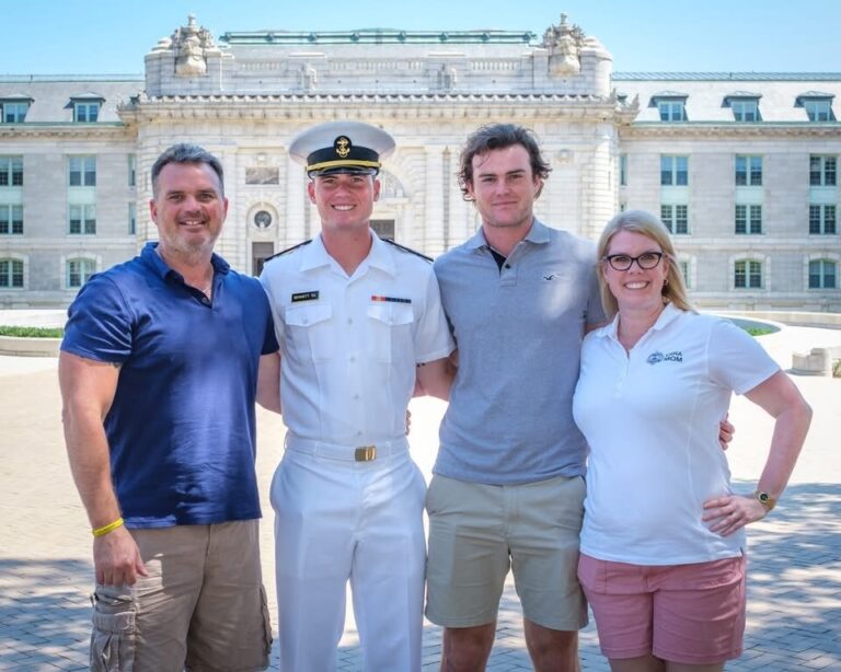 A family standing with a Midshipman in summer whites in front of Bancroft Hall