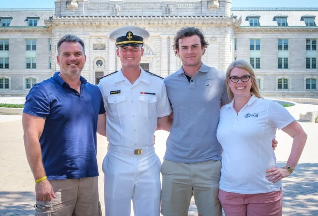 A family standing together with their Midshipman in summer whites in front of Bancroft Hall