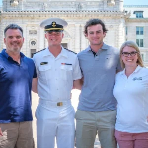 A family standing together with their Midshipman in summer whites in front of Bancroft Hall